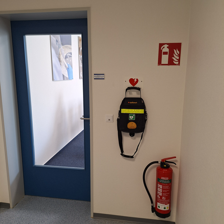 AED in schwarzer Tragetasche an der Wand neben dem Eingang zum Ausbildungsraum, Erdgeschoss (Flur, Raum 504)