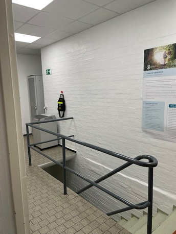 AED in schwarzer Tragetasche an der Wand im Erdgeschoss neben der Kellertreppe und neben Raum 37