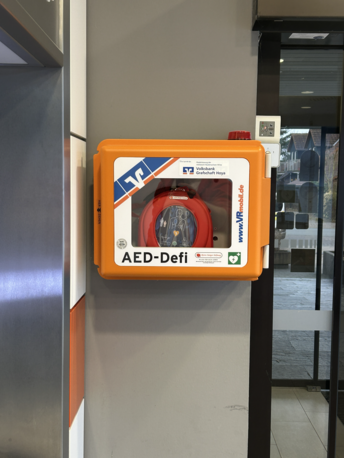 AED im Erdgeschoss im orangenen Wandkasten
