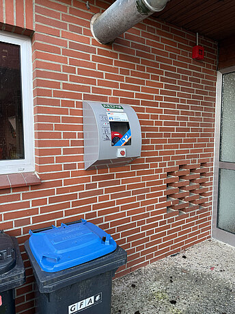 AED im silbernen Wandkasten, links neben der Tür an der Wand des Feuerwehrhauses