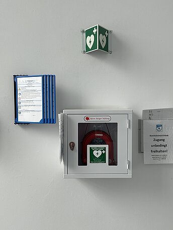 AED im weißen Wandkasten hinter der Eingangstür.