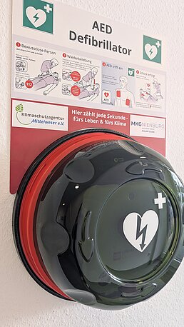 AED im Wandkasten. Runden Deckel drehen und öffnen.