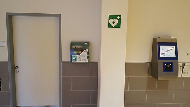 Im Foyer links an der Wand neben dem Hausmeisterraum