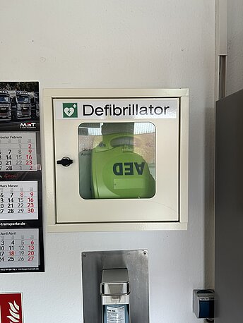 Durch den Eingang; AED im weißen Wandkasten direkt geradeaus. Durch den Eingang; AED im weißen Wandkasten direkt geradeaus.