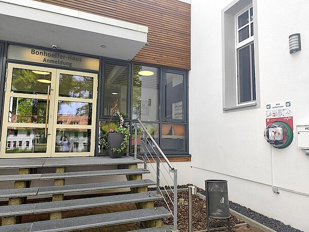 AED im Wandkasten, rechts an der Wand, neben der Treppe zum Eingang Bonhoeffer-Haus/Anmeldung AED im Wandkasten, rechts an der Wand, neben der Treppe zum Eingang Bonhoeffer-Haus/Anmeldung