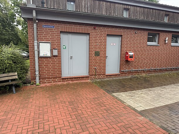 Öffentlicher AED im roten Wandkasten am Feuerwehrhaus, Gebäudeseite des Eingangs, rechts neben der Tür "BMZ"