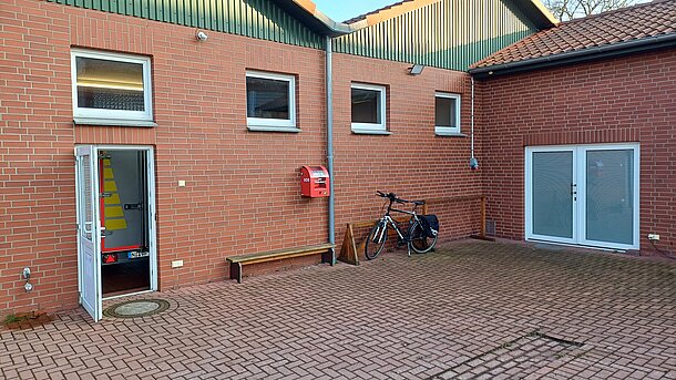 AED im roten Wandkasten am Hintereingang des Feuerwehrhauses auf dem Weg zum Eingang der Sporthalle. AED im roten Wandkasten am Hintereingang des Feuerwehrhauses auf dem Weg zum Eingang der Sporthalle.