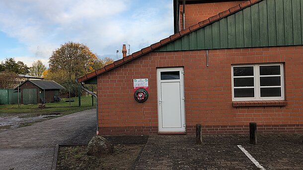 Öffentlicher AED im runden, beleuchteten Wandkasten, an der Gebäudevorderseite/-ecke neben der weißen Tür