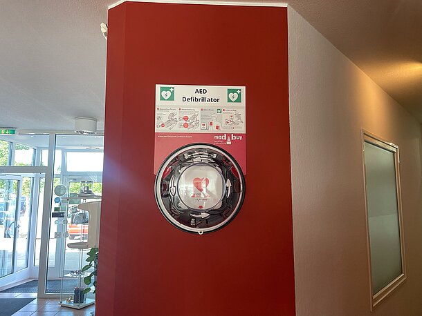 AED im runden Wandkasten an der roten Wand im Durchgangsbereich zu den Herrenumkleiden AED im runden Wandkasten an der roten Wand im Durchgangsbereich zu den Herrenumkleiden