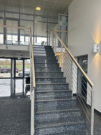 Durch den Haupteingang und der Treppe nach oben folgen. Dann rechts durch die Glastür in das Durchgangsbüro.