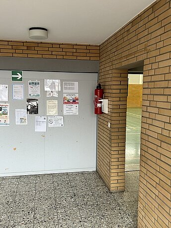 AED links neben dem Durchgang zur Sporthalle an der Wand im Eingangsbereich