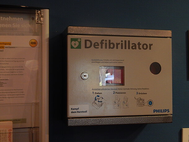 AED hängt an der Wand neben der Informationstafel am Empfangstresen