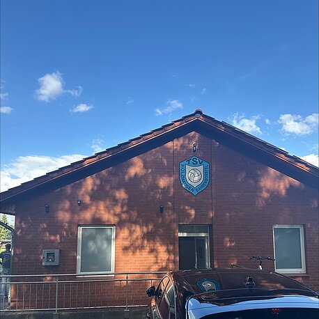 Öffentlicher AED im silbernen Wandkasten, an der Gebäudeseite des Eingangs, linke Gebäudeecke neben dem Fenster