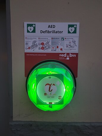 Öffentlicher AED neben dem Nebeneingang an der Gebäuderückseite Öffentlicher AED neben dem Nebeneingang an der Gebäuderückseite