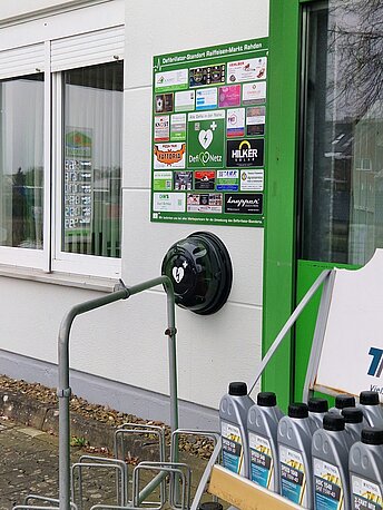 Öffentlicher AED im runden Wandkasten links vom Eingang zum Raiffeisen Markt