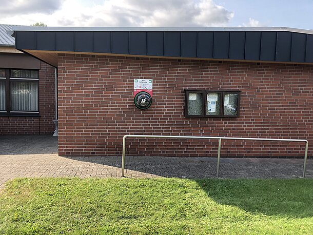 AED im runden, beleuchteten Wandkasten, links neben dem Schaukasten an der Gebäudeseite