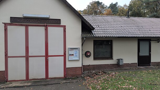 Öffentlicher AED im runden, beleuchteten Wandkasten an der Gebäudeseite zur Straße / um die Gebäudeecke neben den Toren zur Fahrzeughalle der Feuerwehr