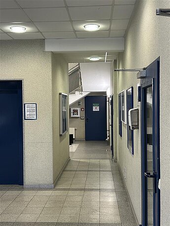 Durch den Haupteingang an der Treppe vorbei hinten an der Wand 