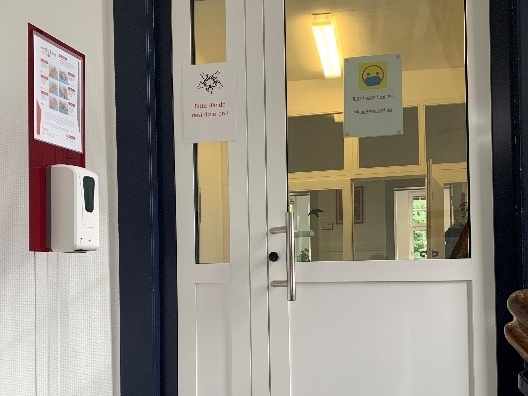 Durch die weiße Zwischentür in den Verwaltungstrakt, wandmontierter AED direkt hinter der Tür links an der Wand